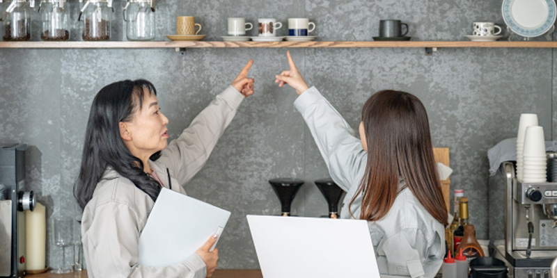 コップを指さして話し合っている飲食店の女性スタッフ2人
