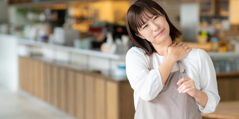肩に手を置いて顔をしかめている女性の飲食店スタッフ