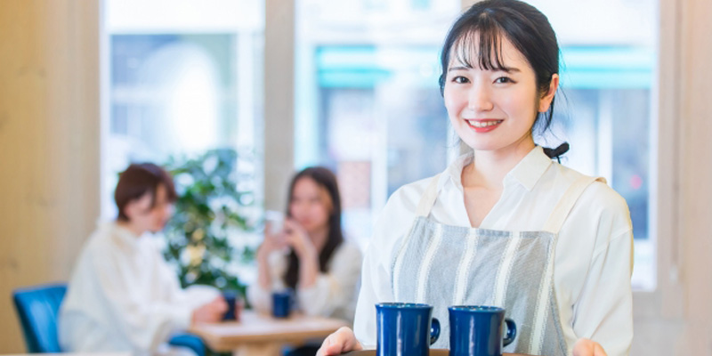 コップが2つのったお盆を持った女性の飲食店スタッフ