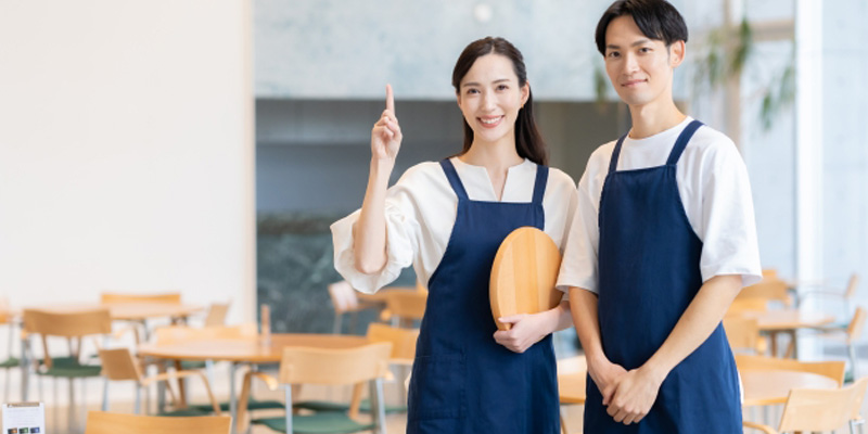 人差し指を立てている女性の飲食店スタッフと両手を前に組んでいる男性スタッフ