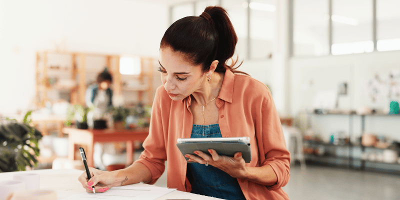 タブレットを見ながら書き物をする女性