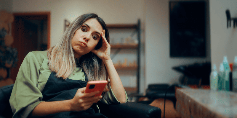 客のいない美容院でスマホを触る女性