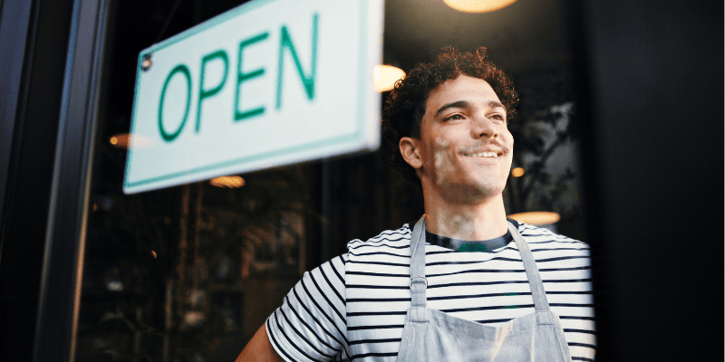 OPENの看板越しの飲食店従業員