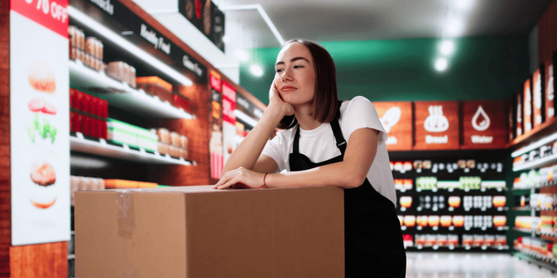 在庫の段ボールの上で考えるスーパーマーケットの従業員